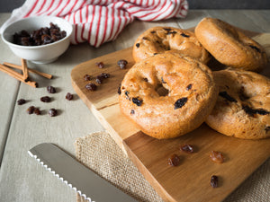 Gluten-free cinnamon raisin bagels from Outside The Breadbox on a wooden board with raisins and cinnamon