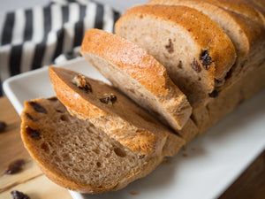 Vegan oat cinnamon raisin gluten-free bread loaf on serving board with cinnamon and raisins