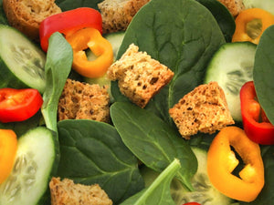 Gluten-free croutons tossed with fresh spinach, cucumber, and sliced bell peppers in a salad